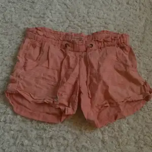 Säljer ett par snygga korallfärgade shorts i linnetyg. De har en elastisk midja och knappar som detaljer. Super bekväma och snygga! 🩷🧡