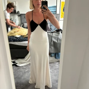 Långklänning massimodutti  - Säljer en elegant svart och vit långklänning med smala axelband och öppen rygg. Klänningen har en stilren design med en tight passform upptill och en flytande kjol. Perfekt för festliga tillfällen eller bal. Oanvänd med prislapp kvar från massimodutti, nypris 2000kr