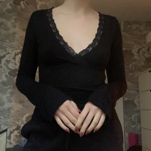 Svart långärmad topp med spetsdetaljer - Snygg svart långärmad topp med v-ringning och spetsdetaljer. Perfekt för både vardag och fest. Den är tight och framhäver figuren på ett smickrande sätt. Passar bra till jeans eller kjol för en stilren look. I storlek xxs men väldigt stretchig så passar snarare xs.