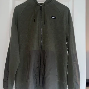 Grön hoodie från Nike - Säljer en grön hoodie från Nike i nyskick. Den har en dragkedja framtill och en justerbar huva med snören. Perfekt för höst och vår. 