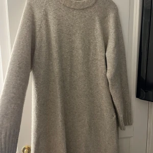 Beige stickad klänning - Mysig och varm beige stickad klänning perfekt för kyligare dagar. Den har långa ärmar och en enkel design som gör den lätt att matcha med olika accessoarer. Perfekt för både vardag och festliga tillfällen!