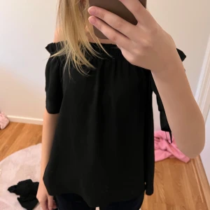 Svart offshoulder topp - Säljer en snygg svart offshoulder topp. Perfekt för en kväll ute eller en avslappnad dag. Toppen är ärmlös och har en lös passform som gör den bekväm att bära.