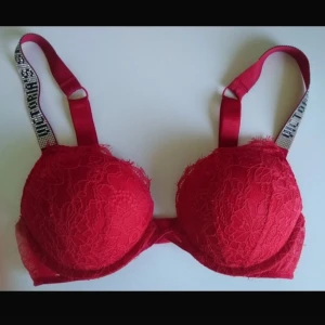 Röd spets-bh med strassdetaljer - Säljer denna Super push-up bh från Victorias secret. Köpte på vinted då enligt säljaren ska den vara använd 2 gånger. Jätte fint skick. Har inte använt den själv då den inte passade. Alla ”stenar” är kvar!!