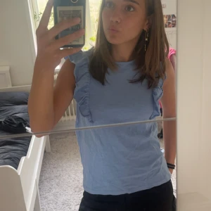 Volang tröja - Ljusblå volang t-shirt, är använd några gånger men fortfarande i bra skick. Storlek 152 eller 11/12 år. Köpt från Mango för några år sedan så vet ej vad nypriset var.