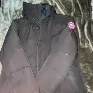 Säljer en svart dunjacka från Canada Goose i storlek L. Jackan är perfekt för kalla vinterdagar och har en snygg broderad logga på ärmen. Den är långärmad och har både dragkedja och knappar för extra skydd mot kylan. Insidan är quiltad för extra värme och komfort. Passar perfekt för vinterns alla äventyr!