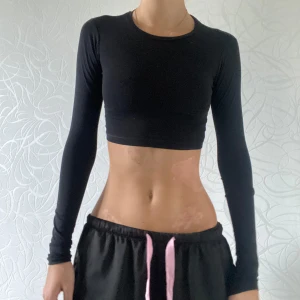 Svart croppad långärmad topp - Säljer en snygg svart croppad topp med långa ärmar. Perfekt för både träning och vardagsbruk. Den är tight och sitter riktigt bra på kroppen. Materialet känns mjukt och stretchigt, vilket gör den superbekväm att ha på sig!