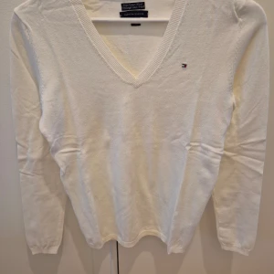 Tröja Tommy Hilfiger - Tröja från Tommy Hilfiger. Vit färg. Nyskick, aldrig använd. V-ringad form. Mjuk och skön material, väldigt bekväm. Märke på höger sida. Storlek XS. 65% bomull, 35% nylon. Axelbredd 36 cm, längd 63 cm.