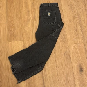 Svarta byxor från Carhartt - Säljer ett par svarta byxor från Carhartt. De har en robust design med förstärkta knän och en avslappnad passform. Perfekta för både arbete och vardag. Byxorna har en klassisk femficksdesign och en dragkedja i gylfen. 