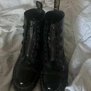 Säljer ett par svarta Dr. Martens boots i lackat skinn. De har en cool dragkedja framtill och klassisk gul söm runt sulan. Perfekta för höst och vinter med sin robusta design och slitstarka material. De har en hög platåsula som ger extra höjd och stil.