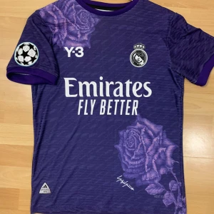 Real Madrid tredje UCL 2023/24 ställ - Säljer en snygg lila fotbollströja från Adidas med Real Madrid-logga och Y-3 design. Tröjan har korta ärmar och ett unikt blommönster i lila nyanser. Riktigt fet tröja med fina detaljer, väldigt bra skick och är väldigt luftig och skön.