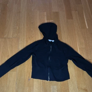 Svart hoodie från H&M - Säljer en svart hoodie från H&M med dragkedja framtill. Den har en bekväm huva och ribbade muddar vid ärmslut och nederkant. Perfekt för en avslappnad stil.