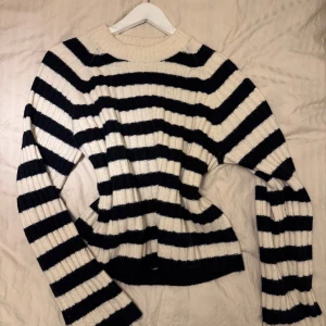 Randig stickad tröja från H&M - Säljer en snygg stickad tröja från H&M i svart och beige med breda ränder. Tröjan har långa ärmar och en rund halsringning. Perfekt för en stilren look!