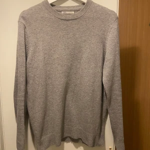Grå tröja från Zara - Säljer en stilren grå tröja från Zara. Den har en klassisk rund hals och långa ärmar, perfekt för kyligare dagar. Tröjan är enkel och passar till det mesta i garderoben.