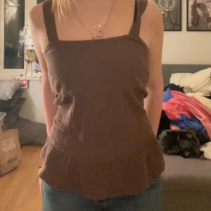 Brun ribbad topp från KappAhl - Säljer en brun ribbad topp från KappAhl i storlek S. Toppen har breda axelband och en fyrkantig halsringning, perfekt för en avslappnad stil.