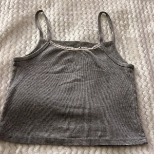 Grå ribbad linnetopp från Brandy Melville - Säljer en stilren grå ribbad linnetopp från Brandy Melville. Toppen har smala axelband och en enkel design som passar perfekt till vardags. Perfekt för lager-på-lager eller att bära som den är.