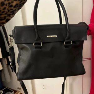 Svart väska från Björn Borg - Snygg svart axelväska från Björn Borg. Väskan har en stilren design med ett metallmärke på framsidan och praktiska fack inuti. 