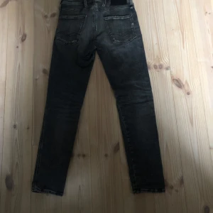 Grå jeans från Replay - Snygga grå jeans från Replay med slitna detaljer och en klassisk femficksdesign. De har en dragkedja och knapp framtill. Perfekta för en avslappnad stil. Passar 175-178 