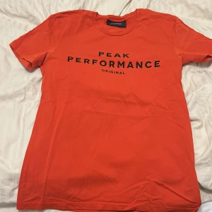 Orange t-shirt från Peak Performance - Snygg orange t-shirt från Peak Performance med svart text på bröstet. Perfekt för en casual look. Gjord i mjukt material för extra komfort.