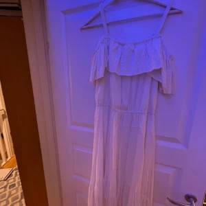 Vit offshoulder klänning - Andvänt 1 gång.Charmig vit offshoulder klänning med volangdetaljer. Perfekt för sommarens festligheter. Klänningen har en luftig passform och är tillverkad i ett lätt material.