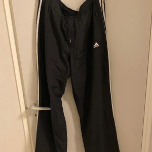 Svarta träningsbyxor/trackpants från Adidas - Säljer ett par svarta träningsbyxor från Adidas. Byxorna har en bekväm passform med resår och snörning i midjan. Perfekta för träning eller en avslappnad dag. Storlek står inte på byxorna men jag skulle säga att det är L/XL