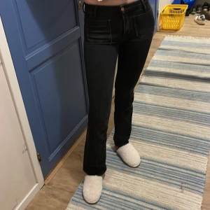 Svarta jeans från Wrangler - Snygga svarta jeans från Wrangler med hög midja och bootcut-stil. De har en klassisk femficksdesign och en diskret logga på bakfickan. Perfekta för en stilren look.