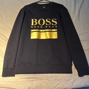 Svart sweatshirt från Hugo Boss - Snygg svart sweatshirt från Hugo Boss med guldtryck på framsidan. 