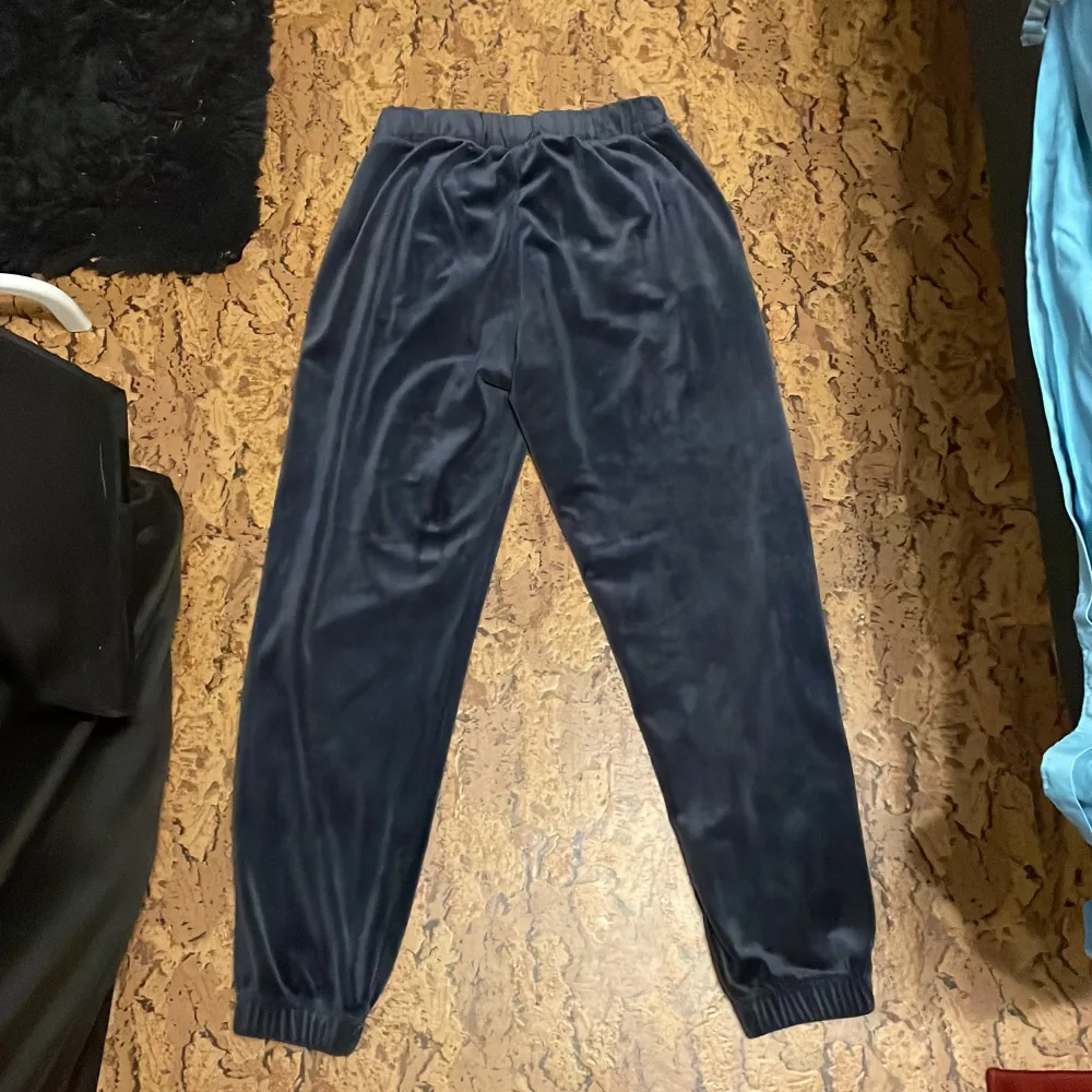 Säljer ett par mörkblå mjukisbyxor i sammet från Lindex med texten 'Believe' i glittriga stenar på sidan. Byxorna har resår i midjan och vid bensluten för extra komfort. Perfekta för en avslappnad men samtidigt festlig stil. Farkut & Housut.
