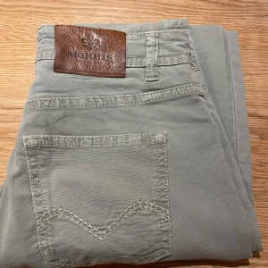 Beige byxor från Morris - Snygga beige byxor från Morris i modellen James Canvas. De har en klassisk design med fem fickor och en läderpatch med logotyp baktill. Perfekta för en stilren look.