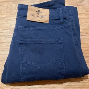 Svarta jeans från Morris - Snygga svarta jeans från Morris med klassisk femficksdesign och knappgylf. Perfekta för en stilren look. Märkesdetaljer på fickan och insidan av midjan ger en exklusiv känsla.