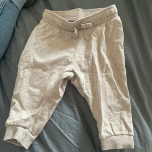 Beige mjukisbyxor för barn - Säljer ett par bekväma beige mjukisbyxor för barn. Byxorna har en elastisk midja med knytband och muddar vid bensluten för extra komfort. Perfekta för lek och mysiga dagar hemma.