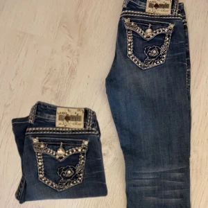Lågmidjade bootcut jeans - Snygga blå jeans från L.A. Idol med unika dekorativa fickor. De har en lågmidjad passform och är utsmyckade med pärlor och broderade detaljer. Perfekta för dig som vill sticka ut med stil.