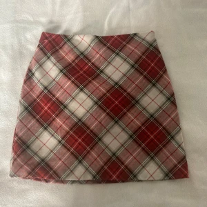 Rutig kjol från H&M - Snygg rutig kjol från H&M i rött, vitt och svart. Kjolen har en klassisk A-linjeform och är perfekt för en trendig look. Den är kort och har en dragkedja i sidan för enkel påklädning. Storlek 36/S.