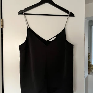 Svart linne med glittriga axelband från H&M - Snyggt svart linne från H&M med glittriga axelband som ger en festlig touch. Perfekt för en utekväll eller speciella tillfällen. Linnet har en enkel och elegant design.