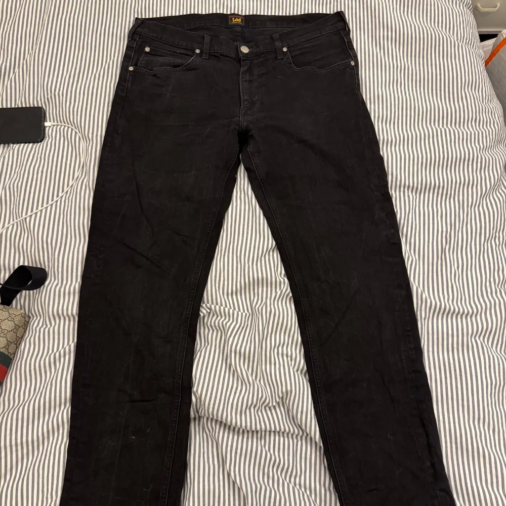 Snygga svarta jeans från Lee med klassisk design och dragkedja. Perfekta för en stilren look. De har en normal passform och är tillverkade i slitstarkt material.. Farkut & Housut.