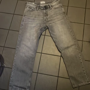 Grå jeans från Jack & Jones - Säljer ett par grå jeans från Jack & Jones i loose fit. De har en klassisk femficksdesign och är perfekta för en avslappnad stil. Passar bra till både sneakers och kängor.