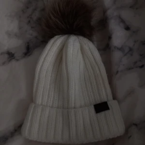 Vit stickad mössa från Sätila - Säljer en superfin vit stickad mössa från Sätila. Den har en stor, fluffig pälsboll på toppen och en ribbad design. Har använt den 3-5 gånger bara då jag sen började tröttna på den. Mössan är mer krämvit än kritvit om någon fattar vad jag menar!