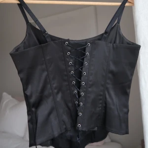 Svart korsettopp  - Glansigt svart material. Dragkedja som är dold i sidan. 