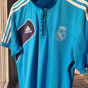 Real Madrid fotbollströja från Adidas - Säljer en snygg blå Real Madrid fotbollströja från Adidas. Den har en stilren design med klubbens emblem på bröstet och Adidas-loggan på sidan.  100% Authentic 
