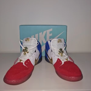 Nike Dunk High Premium SB - Säljer ett par riktigt sällsynta coola Nike Dunk SB sneakers i färgerna röd, blå och vit med snygga gulddetaljer, ice bottom. Skorna har en unik design med en mix av mocka och skinn, och de har snörning av läder. Perfekta för att sticka ut i mängden!