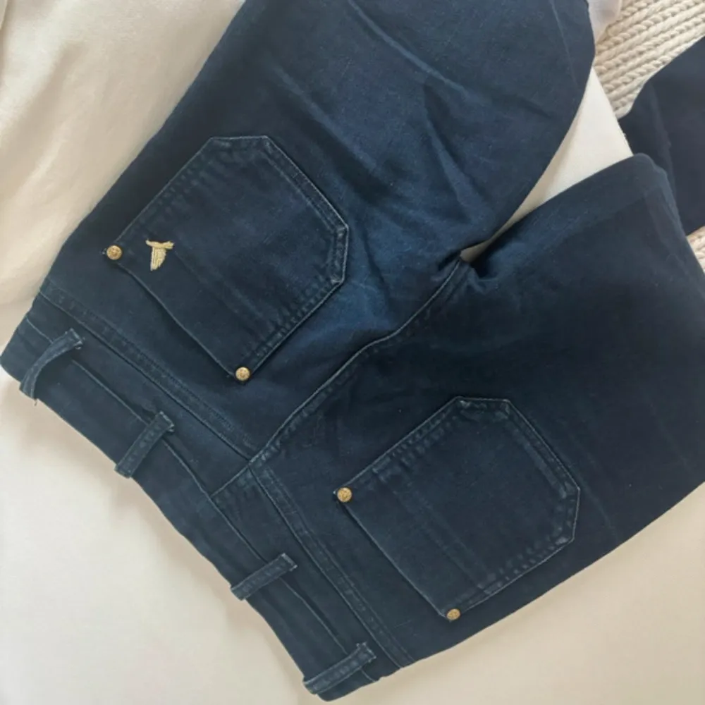 Säljer ett par snygga mörkblå bootcut jeans från MiH Jeans. De är högmidjade och har en klassisk femficksdesign med guldiga knappar och dragkedja. Perfekta för både vardag och fest!. Farkut & Housut.