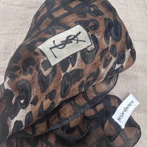 YSL Leopard Silk Scarf - Beautiful rectangle silk leopard print scarf. You can use it on the lapel of your jacket or in a scrunchie as a hair accessory and even tied on a business bag. Very versatile :) It does have 2 flaws. A small tear and stain. Not visible when on. 