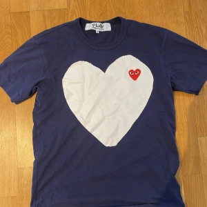 Cdg tisha - Säljer denna feta Cdg tisha, condition är 8/10 lite av de vita har gått bort från hjärtat som ni ser på andra bilden, Storlek S passar 17-178 skriv till mig gällande pris!