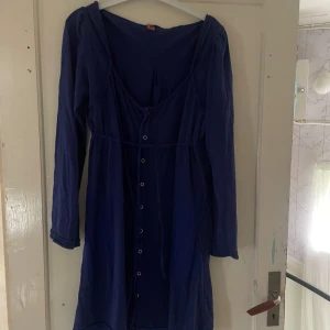 Blå klänning med knappar - Säljer en snygg blå klänning med knappar framtill. Den har långa ärmar och en bekväm passform som passar perfekt för både vardag och fest. Klänningen är i ett mjukt material och har en fin v-ringad design.