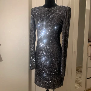 Glittrig svart klänning - Säljer en superglittrig svart klänning som verkligen fångar ljuset! Den är långärmad och perfekt för en fest eller nyårsafton. Klänningen har en tight passform som framhäver figuren och är täckt av glittriga paljetter. Ett måste för den som vill sticka ut!