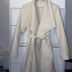 Beige/ vit kappa - En vacker crémefärgad kappa i utmärkt skick. Denna tidlösa kappa är perfekt för både vardag och fest, och har endast använts ett par gånger. Den är lätt att kombinera med olika outfits och ger en elegant look. Kappan är i storlek 36/S. 