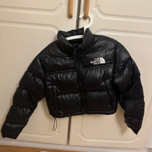 Svart pufferjacka från The North Face - Säljer en snygg och varm svart pufferjacka från The North Face Nupts croppad  Perfekt för kalla dagar när du vill hålla stilen. Den är i super bra skick och kvittot finns med !