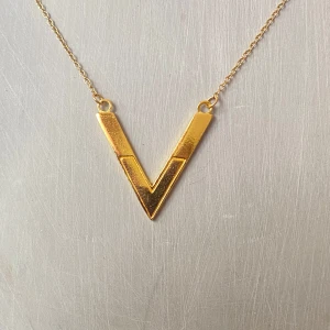 Guldigt V-format halsband från Gorjana - Säljer ett stilrent och elegant V-format halsband i guld från Gorjana. Halsbandet har en tunn kedja och en minimalistisk design som passar perfekt till både vardag och fest. Det är i nyskick och har en liten rund bricka med märkets namn vid låset.