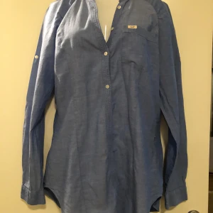 Blå henley-skjorta från KB Lee - Säljer en snygg blå henley-skjorta från KB Lee i storlek M. Skjortan är tillverkad i 100% bomull och har långa ärmar med knappar. Perfekt för både vardag och fest! 💙