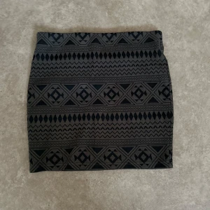 Svart och grå mönstrad kjol - Säljer en snygg svart och grå kortkjol med geometriskt mönster. Perfekt för både vardag och fest! Kjolen har en tight passform som framhäver figuren. Materialet känns mjukt och stretchigt, vilket gör den bekväm att bära hela dagen. Passar perfekt till en enkel topp eller en stickad tröja för en mer avslappnad look.