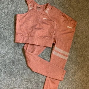Träningstopp + byxor från Stronger - Säljer en snygg roströd tights + tillhörande träningstopp från Stronger. Toppen är ärmlös och har precis som tightsen en tight passform, perfekt för gymmet eller yoga. Den är gjord i ett mjukt och stretchigt material som andas bra. Båda är i mycket bra skick och endast använda ett fåtal gånger.